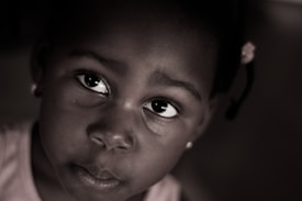 A close-up portrait of a young child gazing upwards. The image is in a sepia tone with soft lighting that emphasizes the child's expressive eyes. A subtle focus on the emotions conveyed through the child's facial expression.