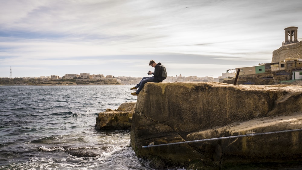 Hombre sentado en la roca marrón cerca del mar durante el día