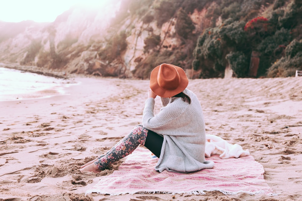 photo of person sitting on sand at seashore