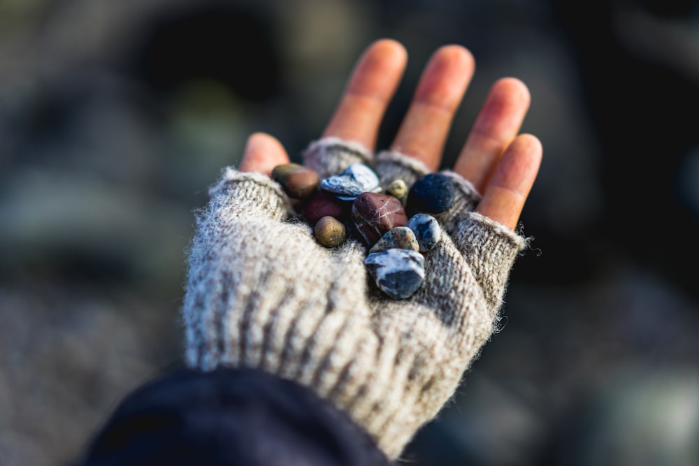 돌을 들고 있는 회색 니트 손가락 없는 장갑을 착용한 사람의 선택적 초점 사진