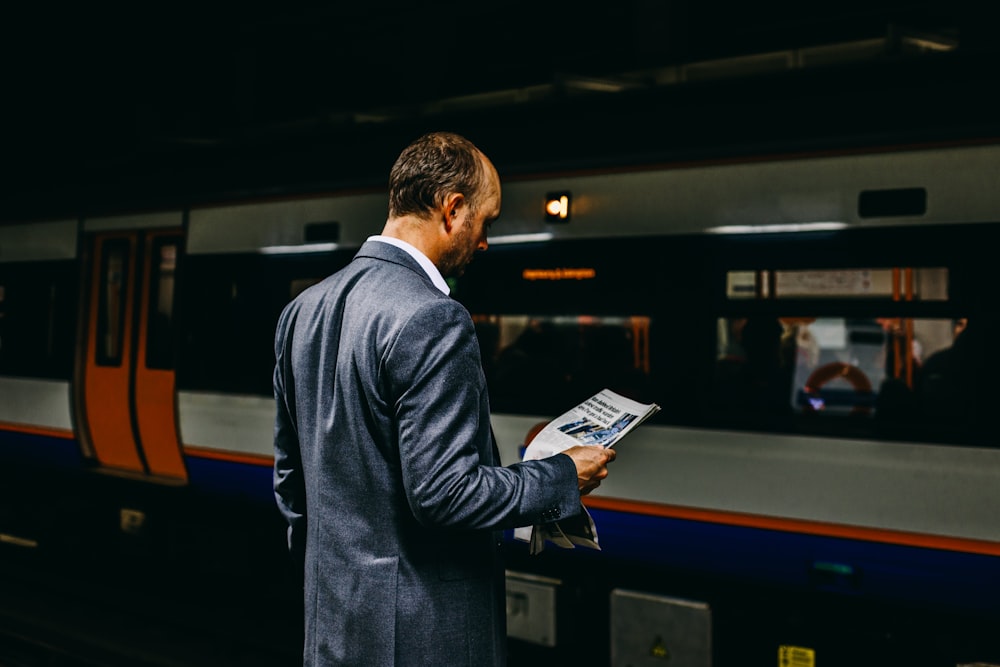man holding newspaper standing on train station
