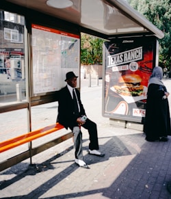 man sitting on orange bench beside woman standing