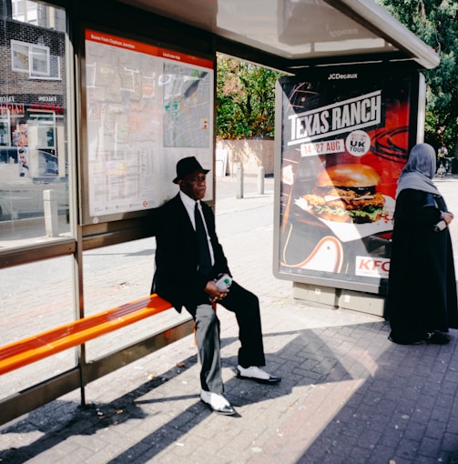 man sitting on orange bench beside woman standing