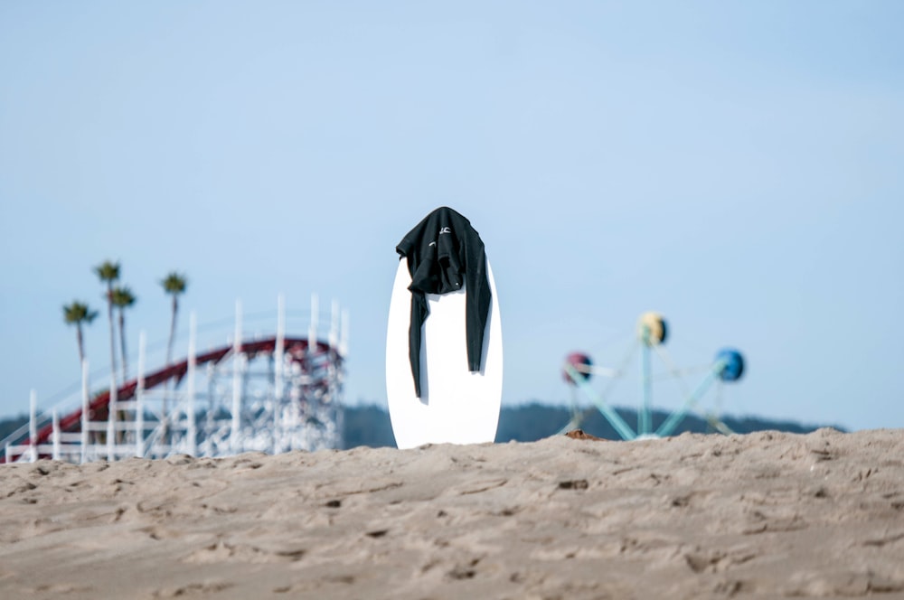 prancha de surf branca com rashguard preto no topo no meio da areia