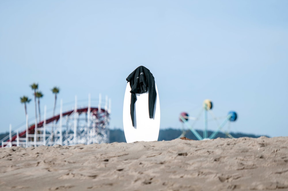 white surfboard with black rashguard on top in the middle of sand