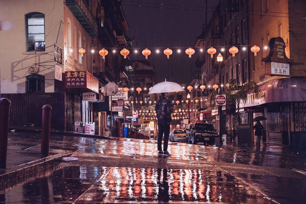 Persona in piedi sulla strada che tiene l'ombrello durante la notte