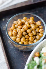A bottle of gosattuu surrounded by roasted chickpeas and fresh green leaves on a cream background.