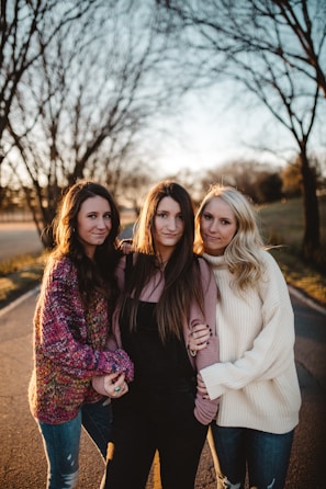 shallow focus photography of three women standing along trees