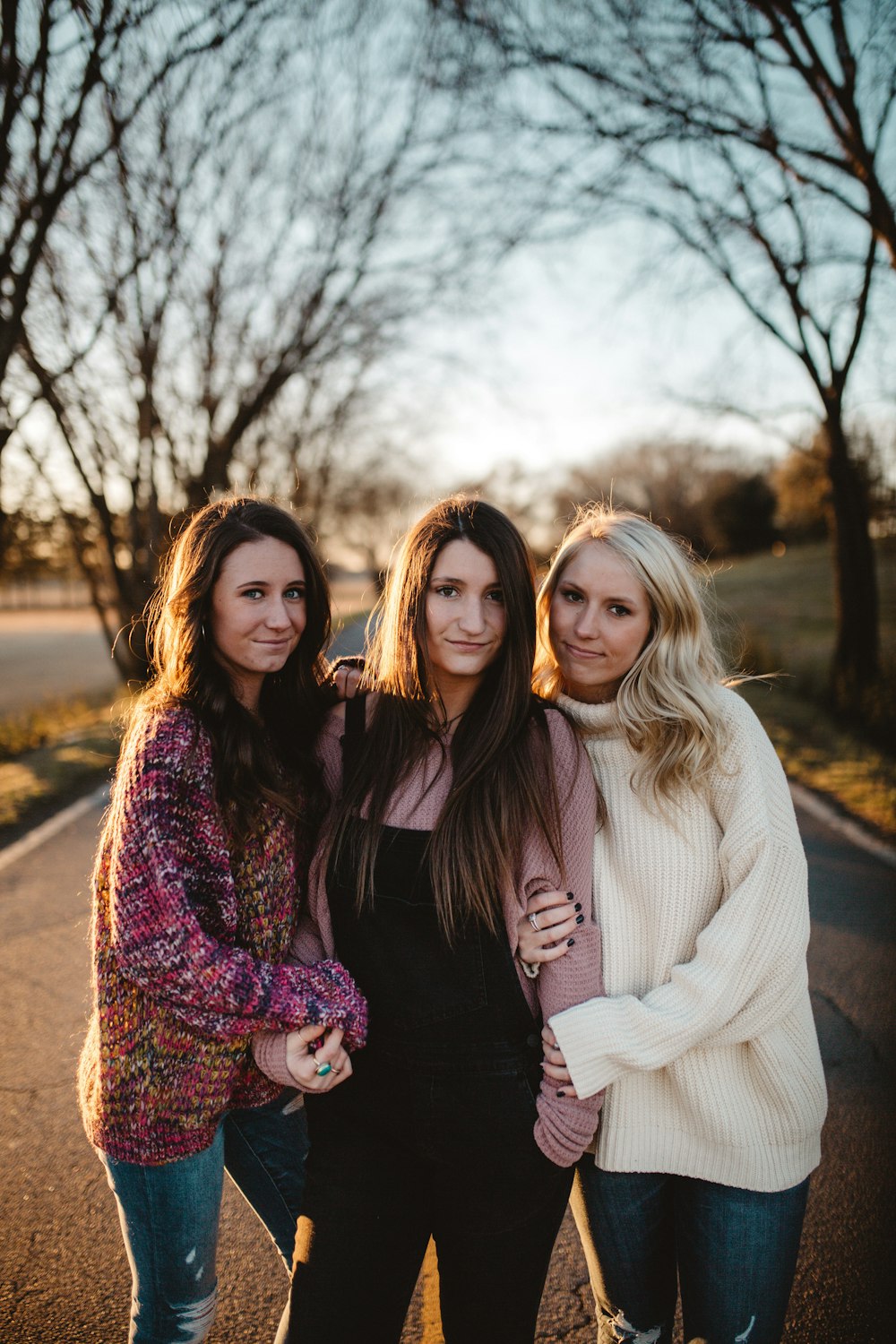 shallow focus photography of three women standing along trees