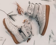 Overhead shot of a pair of brown oxfords next to a small pine cone on a pebble surface.