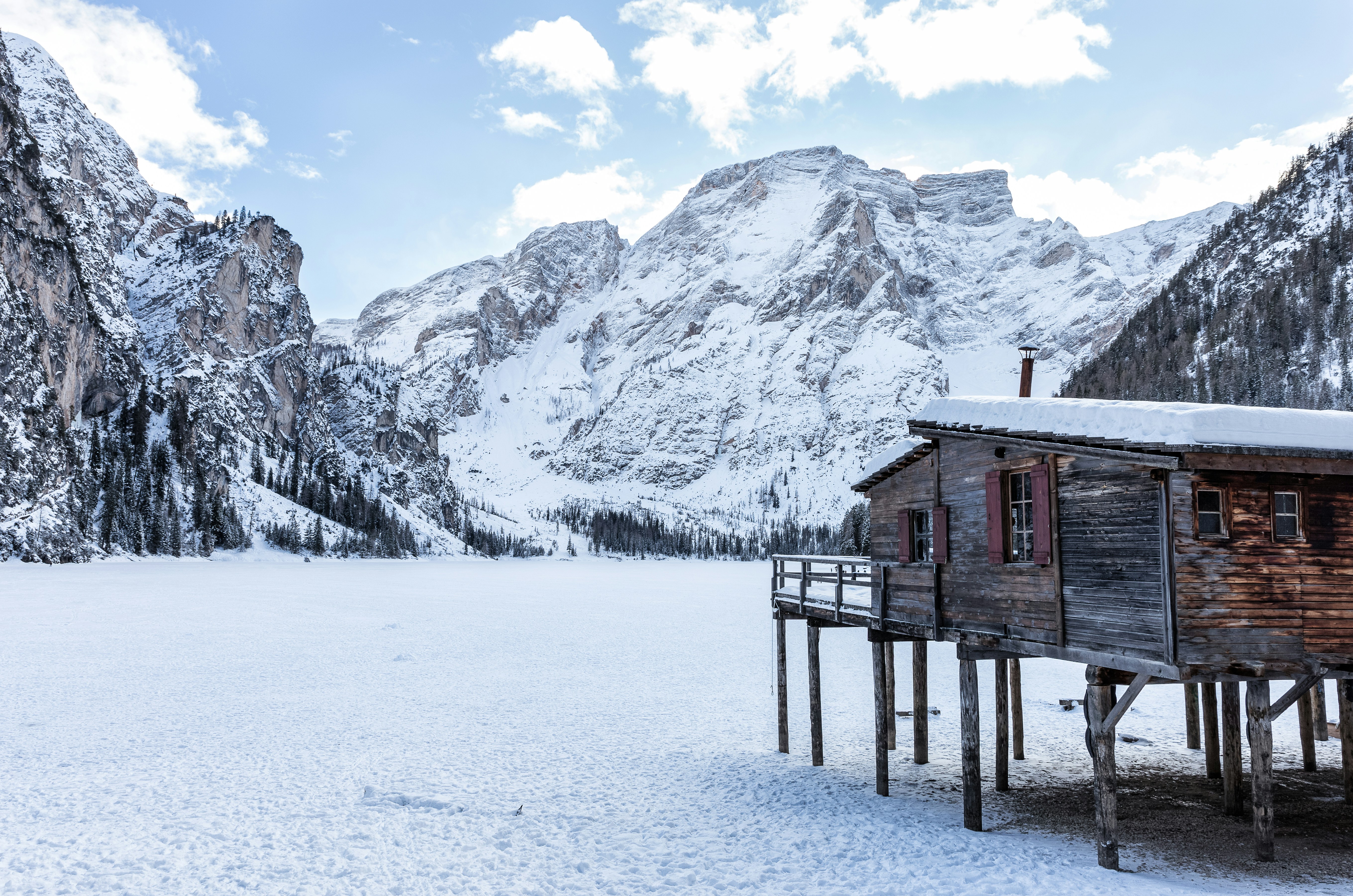 brown wooden house near mountains covered with snow at daytime, Lake Braies completely frozen.