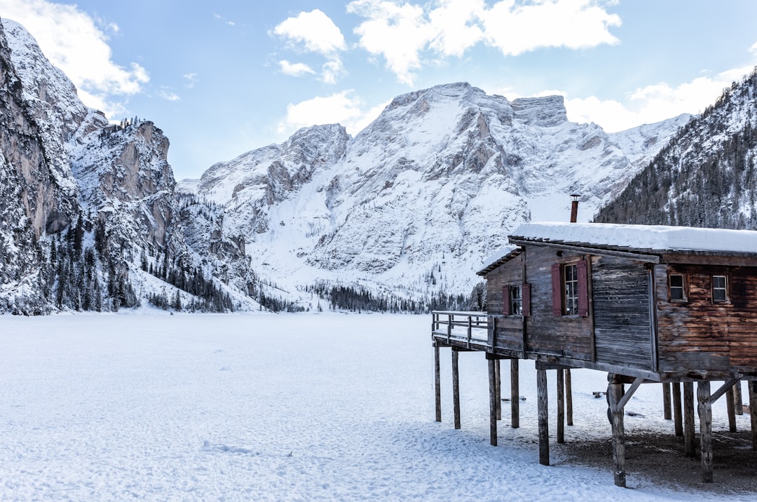 brown wooden house near mountains covered with snow at daytime, Lake Braies completely frozen.