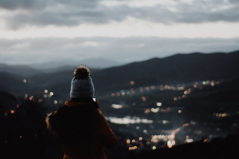 person standing on cliff with city lights as view