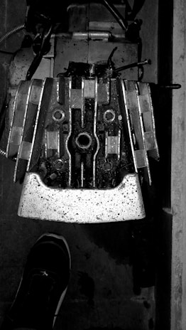 A close-up view of a mechanical component with a shoe visible at the bottom part of the image. The component appears metallic with several bolts and intricate patterns, suggesting it might be part of a larger machine or engine.
