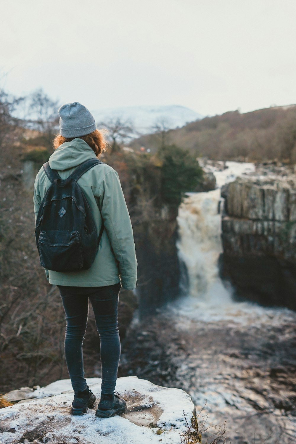 woman standing on cliff facing waterfall