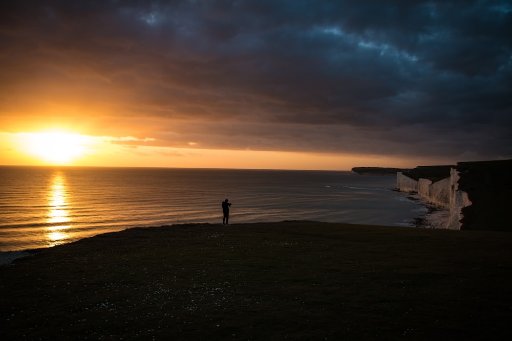 silhouette photography of person standing in front of body of water