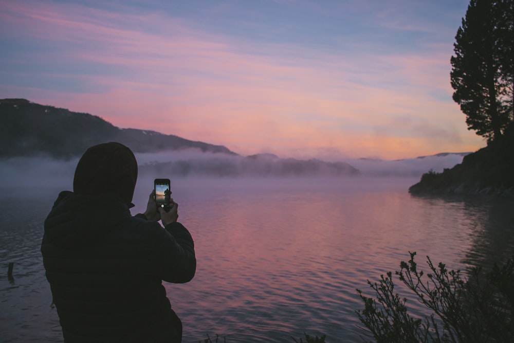 person taking photo of foggy river