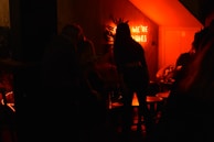 A cozy corner of the private studio with drinks and game night setup, glowing warmly under pink neon lights.