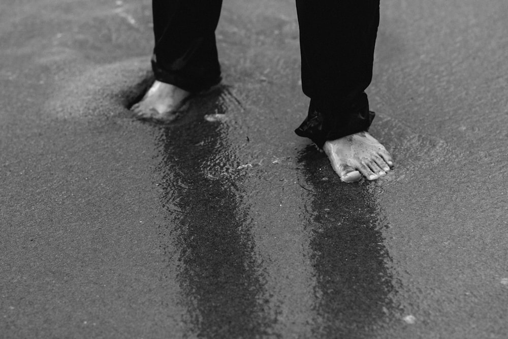 barefooted person wearing pants standing on wet sand