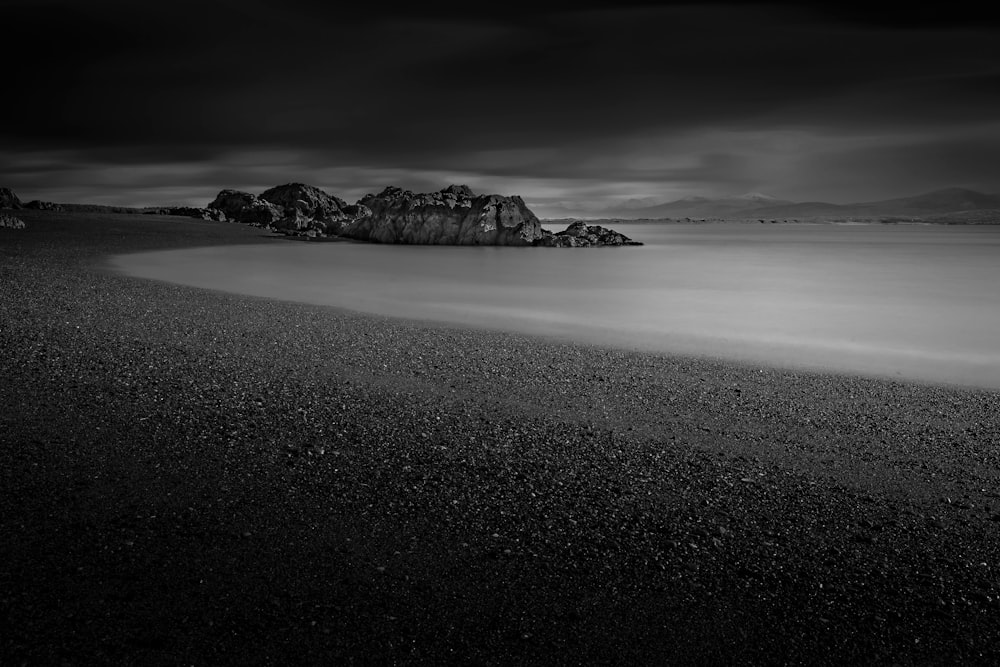 grayscale photography of body of water near mountain