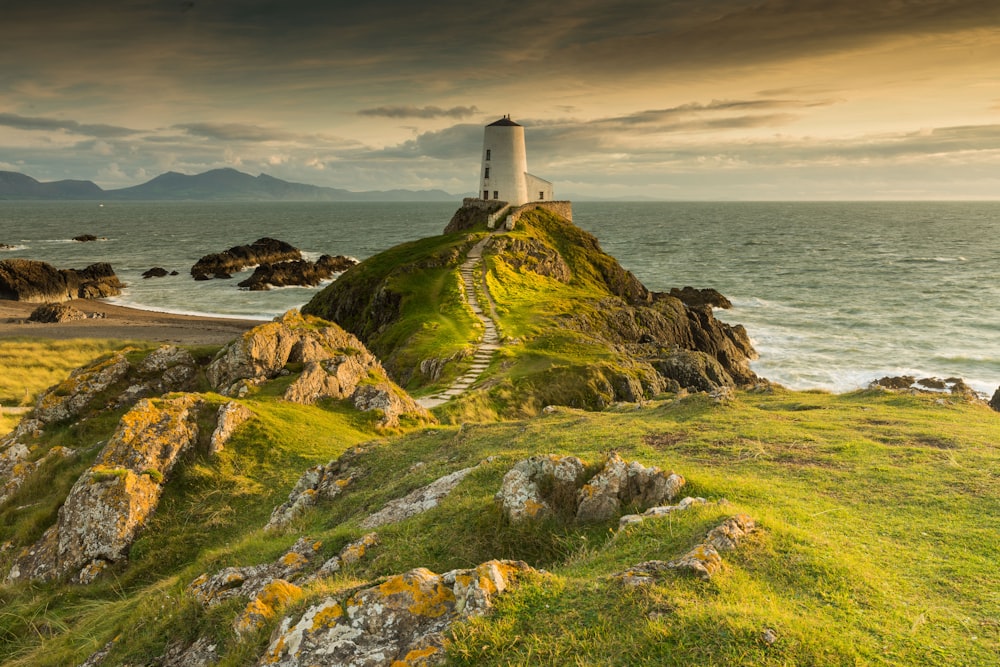 white concrete lighthouse on cliff beside sea under clear blue sky during daytime