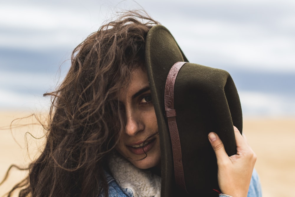 Donna che tiene il cappello nero in riva al mare durante il giorno