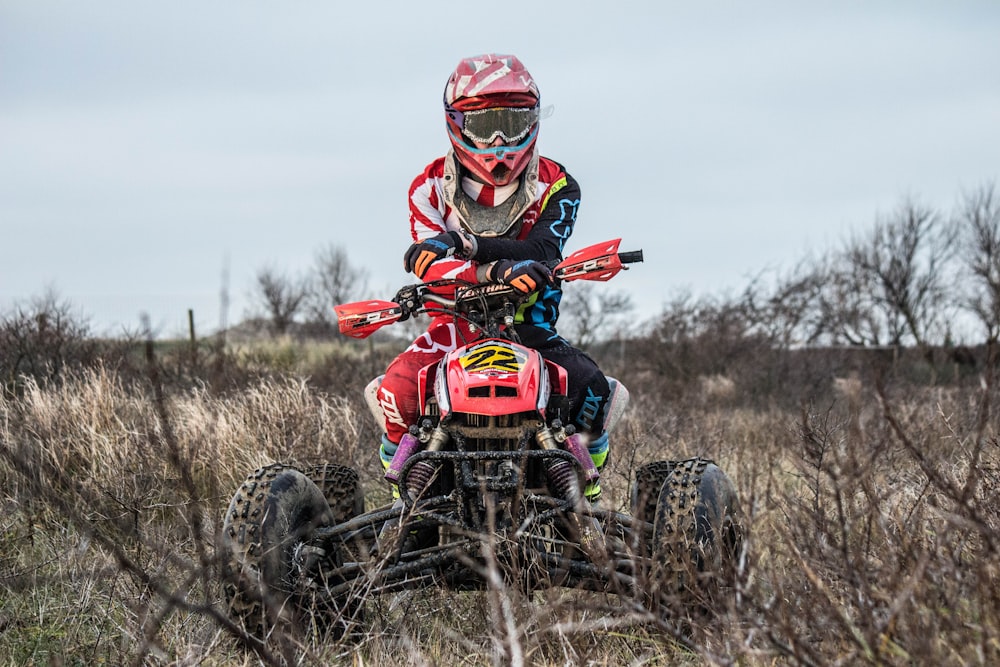 a man riding a red four - wheeler through a grass covered field