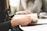 A close-up of a person holding a book while engaging in reading or study. Another person is sitting nearby, both seemingly focused on their tasks. The setting suggests a studious or collaborative environment, possibly at a library or study room.