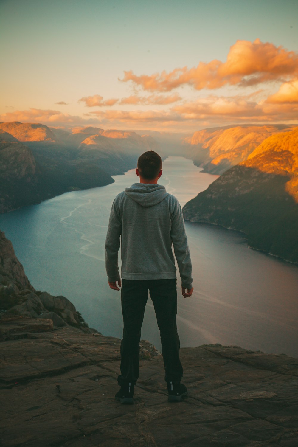Mann im grauen Kapuzenpullover steht auf dem Berg und schaut auf den Fluss