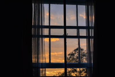 A serene photo of a sunset viewed through a sheer rose-colored curtain.