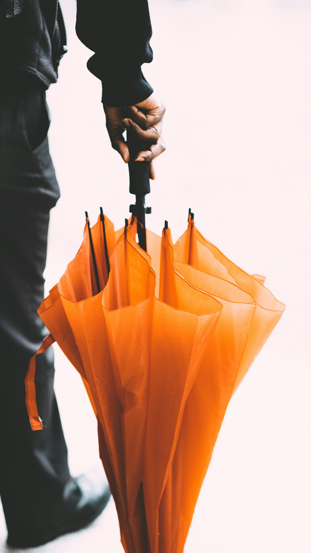 person in black pants standing and holding orange umbrella on right hand