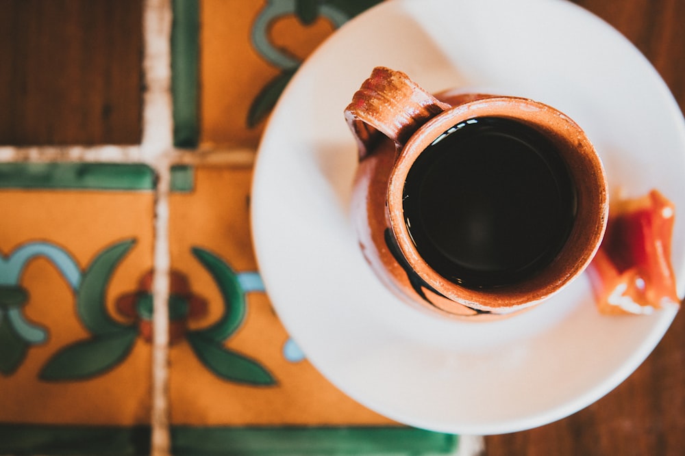 brown ceramic mug with coffee on white ceramic saucer