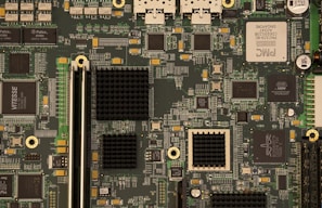 A detailed view of a computer motherboard with various integrated circuits and components including chips, capacitors, and connectors. The board is densely populated with intricate pathways and electronic parts, indicative of complex technology.