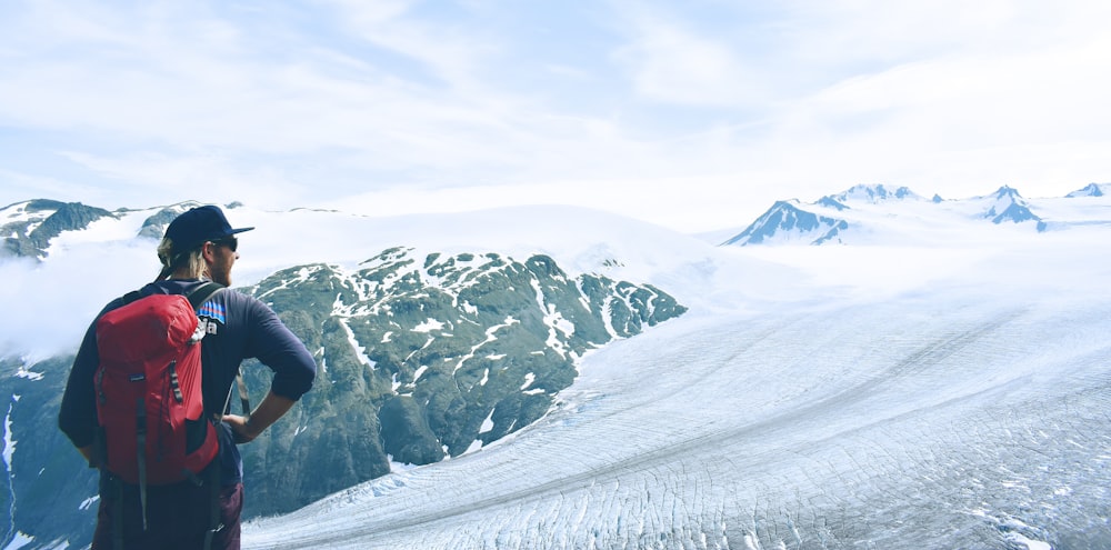 man in red backpack standing on snowy land