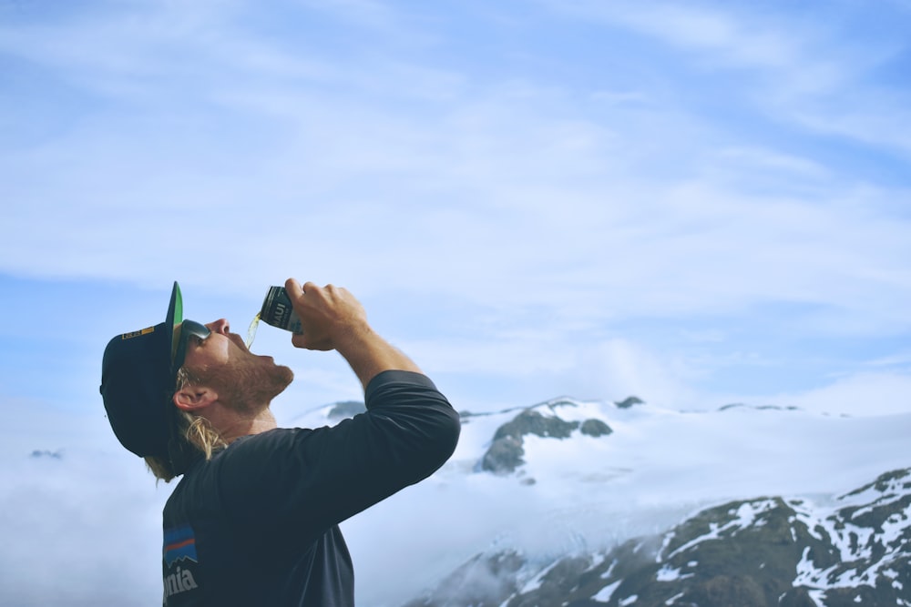 person drinking beverage in front of mountain covered by clouds
