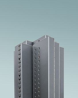 A high-rise building with a modern design, featuring a sleek, grey exterior with numerous small windows. The building stands tall against a light, clear sky, creating a minimalistic and clean visual.
