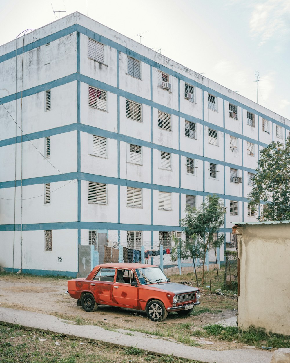 red car parked in front of white concrete building during daytime