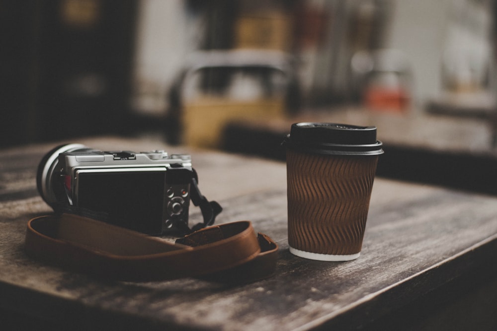 gray DSLR camera beside brown plastic cup