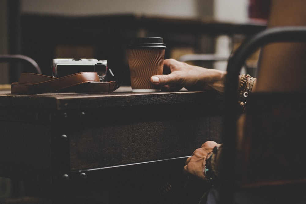 person holding gray plastic cup on table