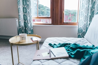 quilted white mattress with spiral notebook and green comforter beside round yellow end table inside room