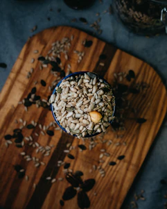 Close-up of a variety of bird seeds artfully arranged on a natural wooden surface with soft, warm lighting.