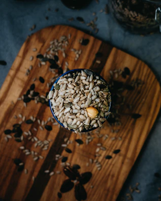 Sunflower seeds spilling from a rustic wooden bowl on a weathered table.