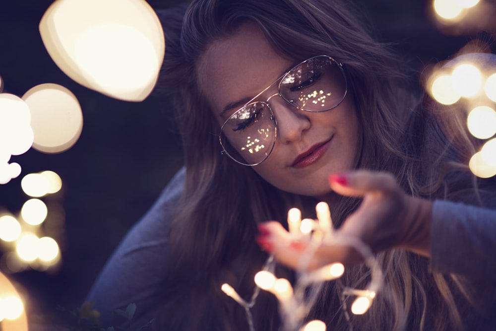 woman in blue tops wearing eyeglasses holding string lights