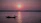 A small group of friends smiling on a boat deck with a sunset over the ocean behind them.