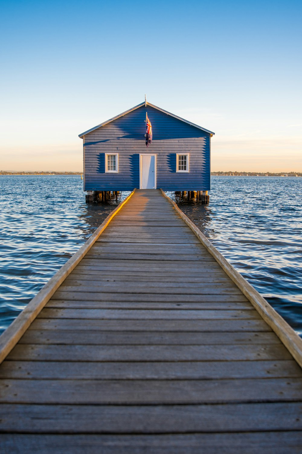 昼間の澄み切った青空の下、海に浮かぶ青と白の木造家屋