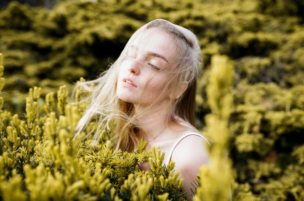 woman wearing white spaghetti strap top standing near yellow petaled flower