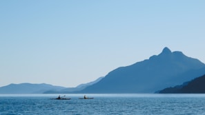 Kayakers paddling through calm blue waters with the Andes mountains in the background under a clear sky