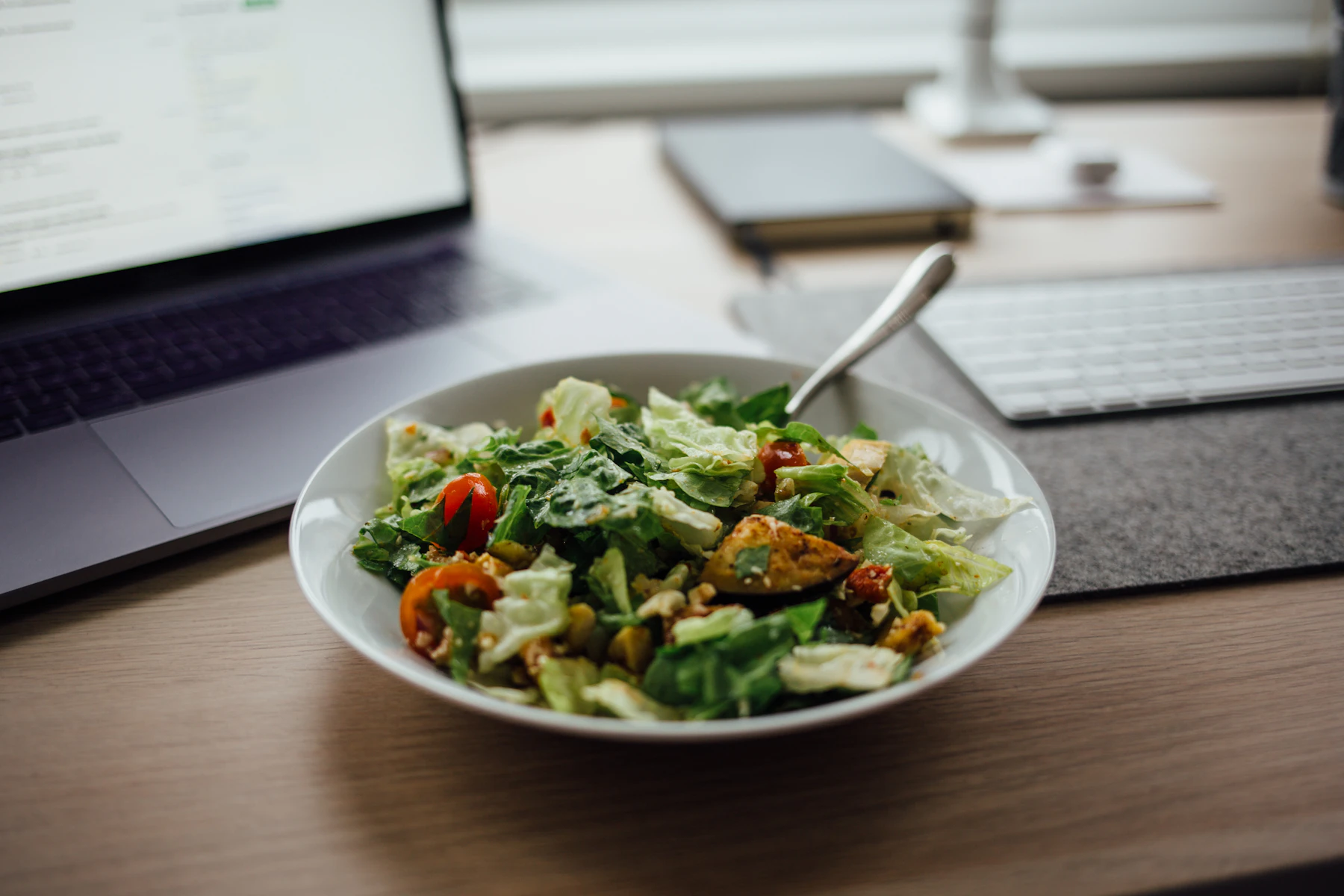 Ensalada junto a un portátil y una libreta sobre una mesa de trabajo