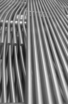 A collection of metallic pipes aligned in parallel and creating a pattern of curves and lines, giving a sense of industrial design.