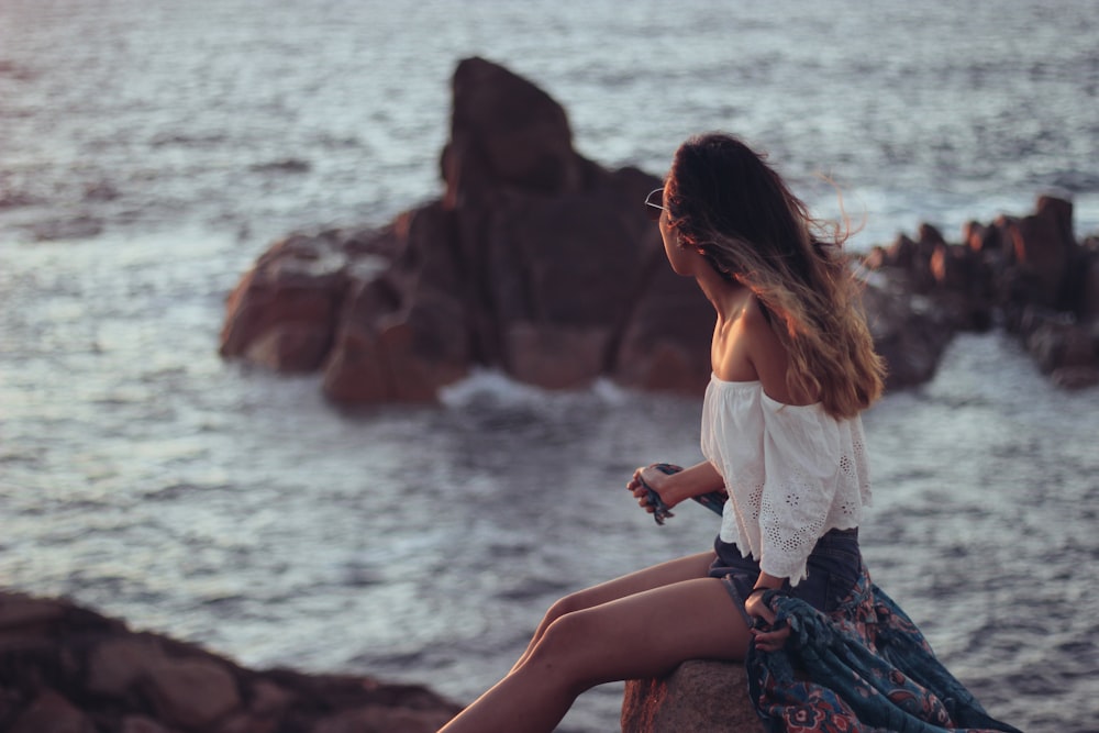 woman in white top sitting near body of water